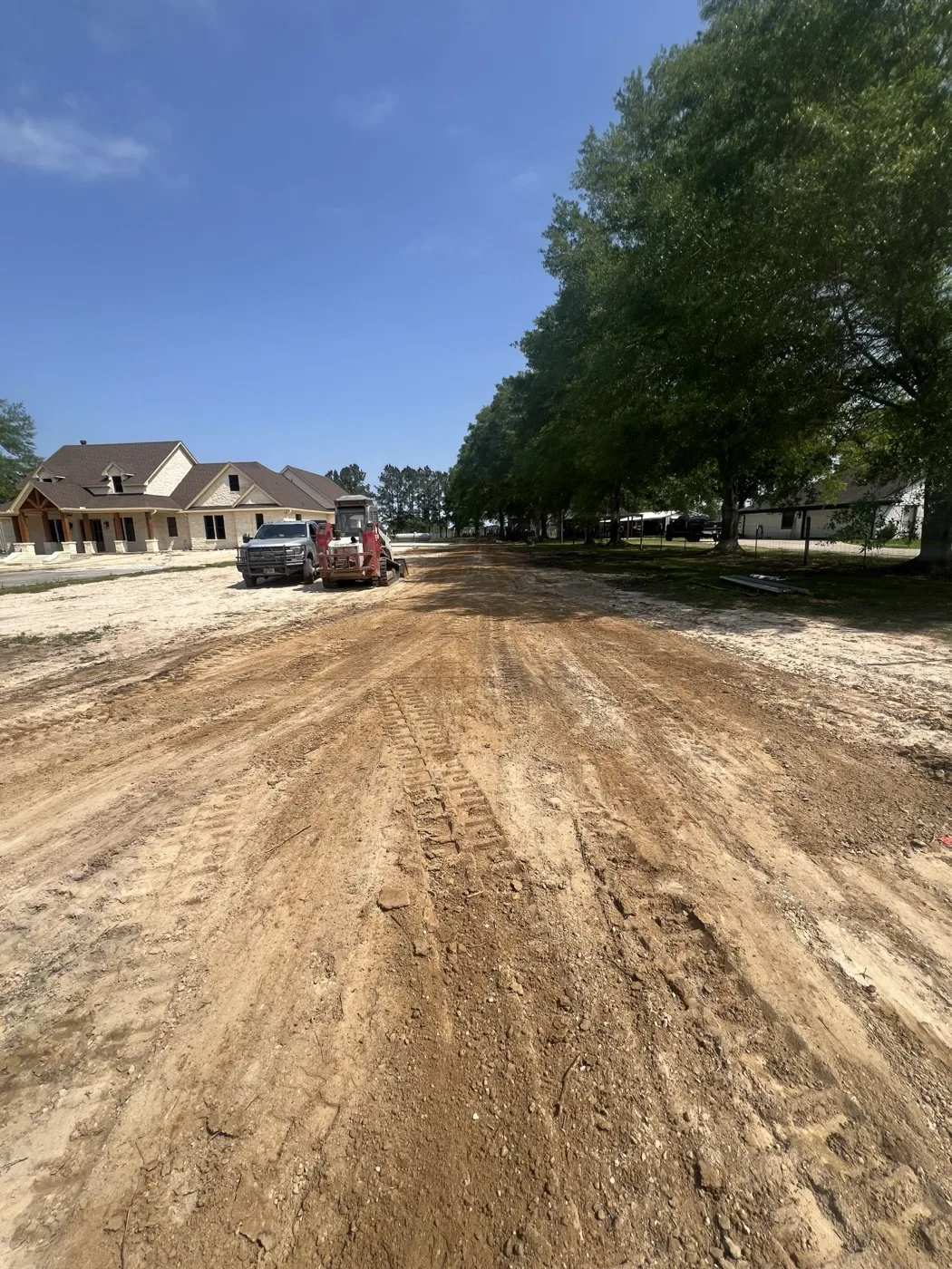 Wide dirt drive being graded with equipment working near new homes