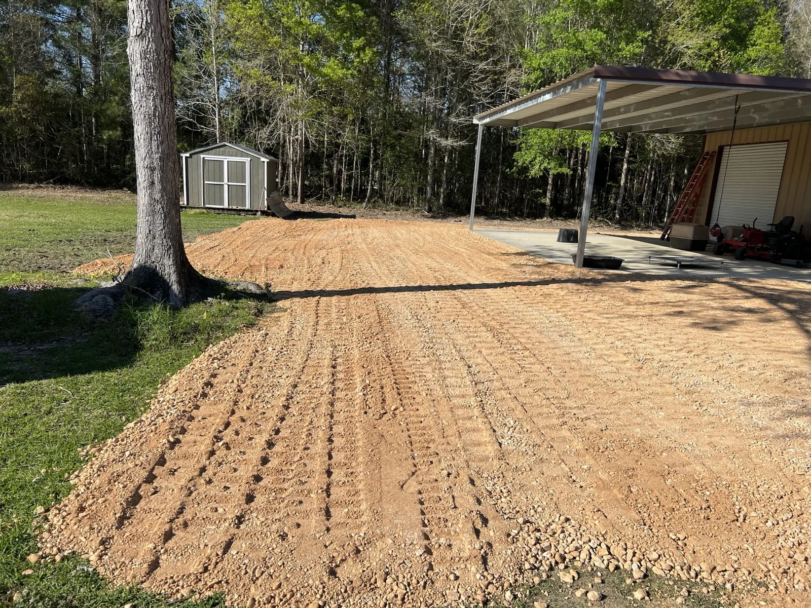 Fresh gravel driveway spread beside a shop and carport