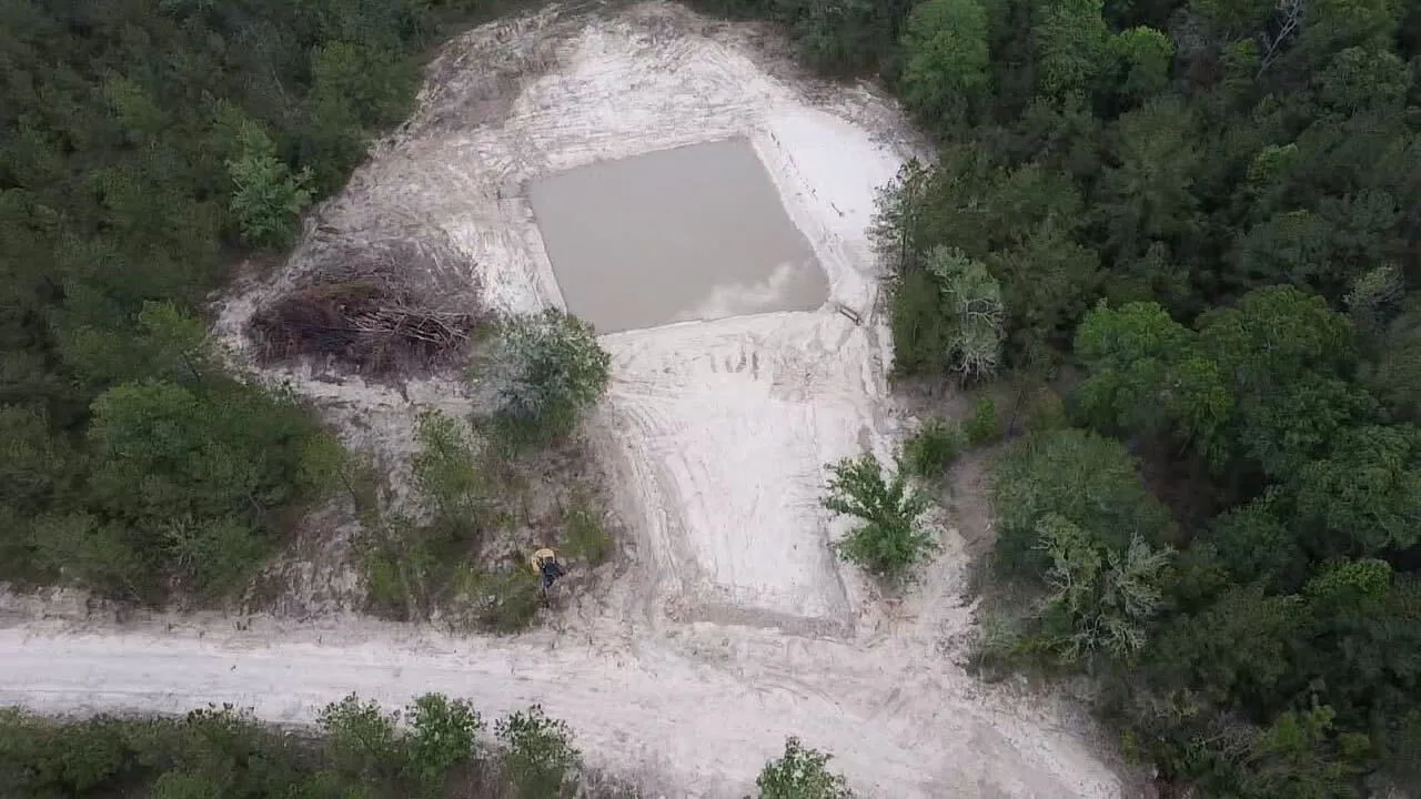 Aerial view of a newly built pond holding water with shaped sandy banks, cut out of the pines with a brush pile at the water's edge